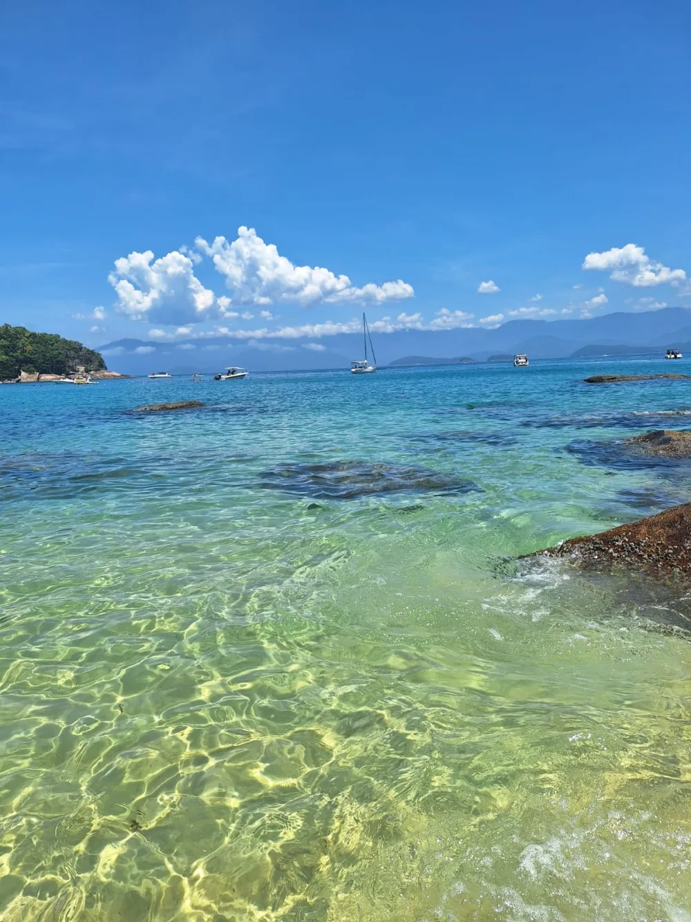 Mar transparente com veleiro e montanhas ao fundo